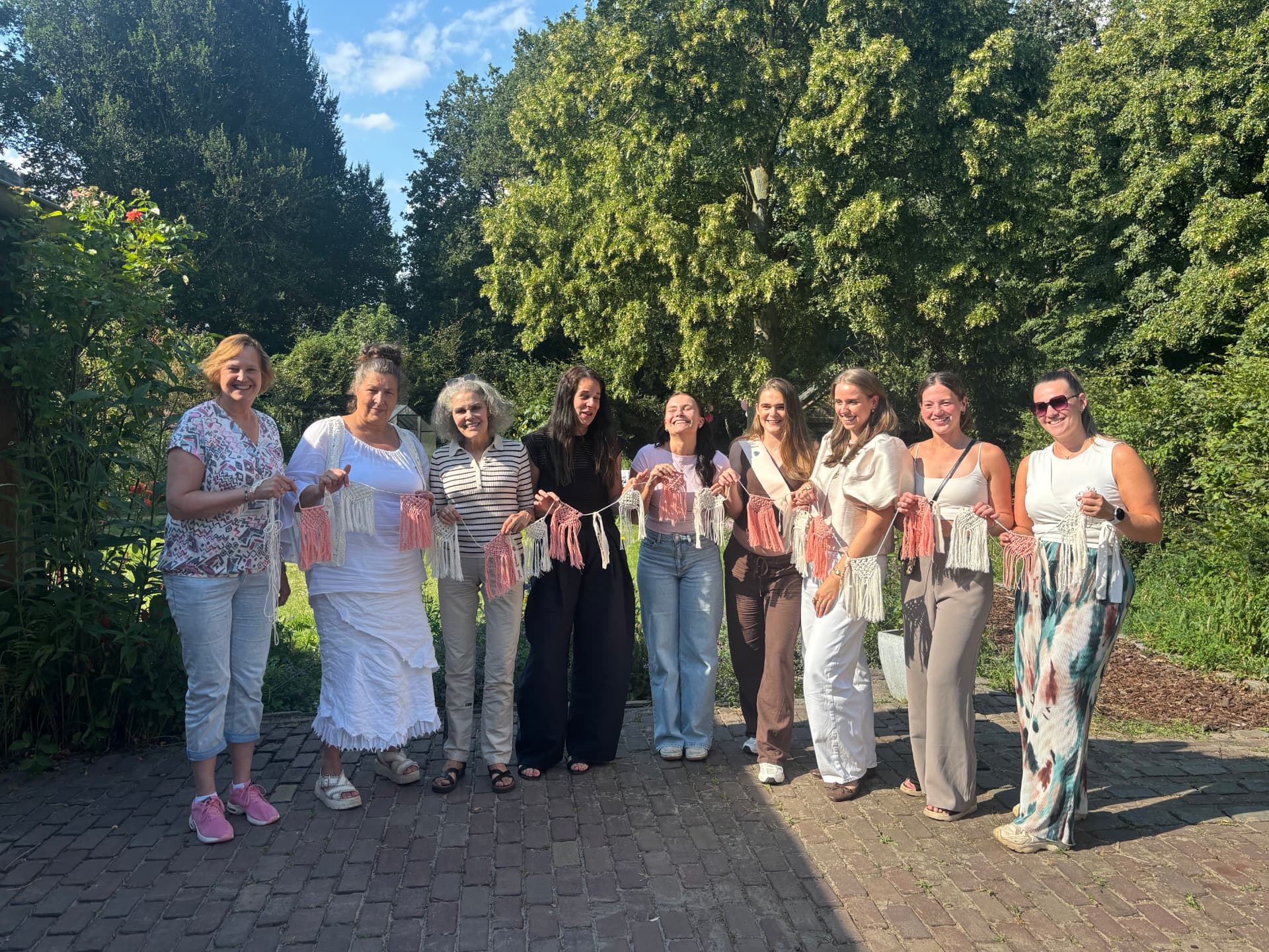 Groep lachende vrouwen in de tuin met hun zelfgemaakte macramé slingers