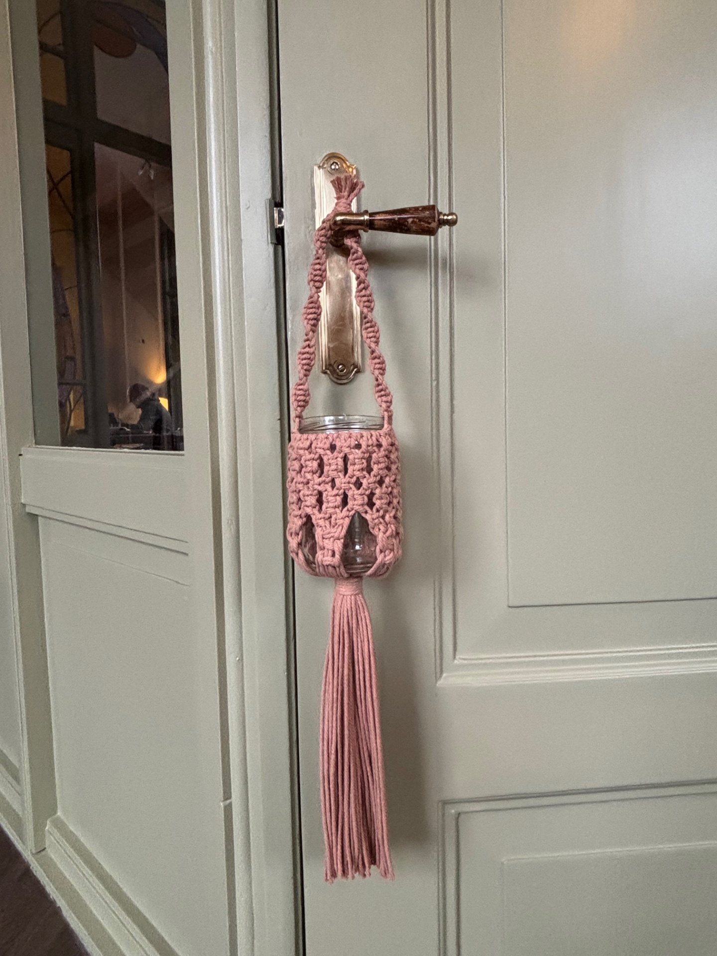 Roze macramé windlichthouder met kwast aan een deurklink